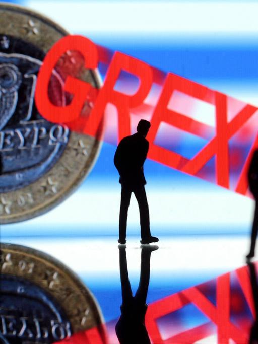 Ungewisse Zukunft Griechenlands: nachdenkliche Manager Figuren stehen vor griechischer Flagge und griechischem Euro mit Schriftzug Grexit