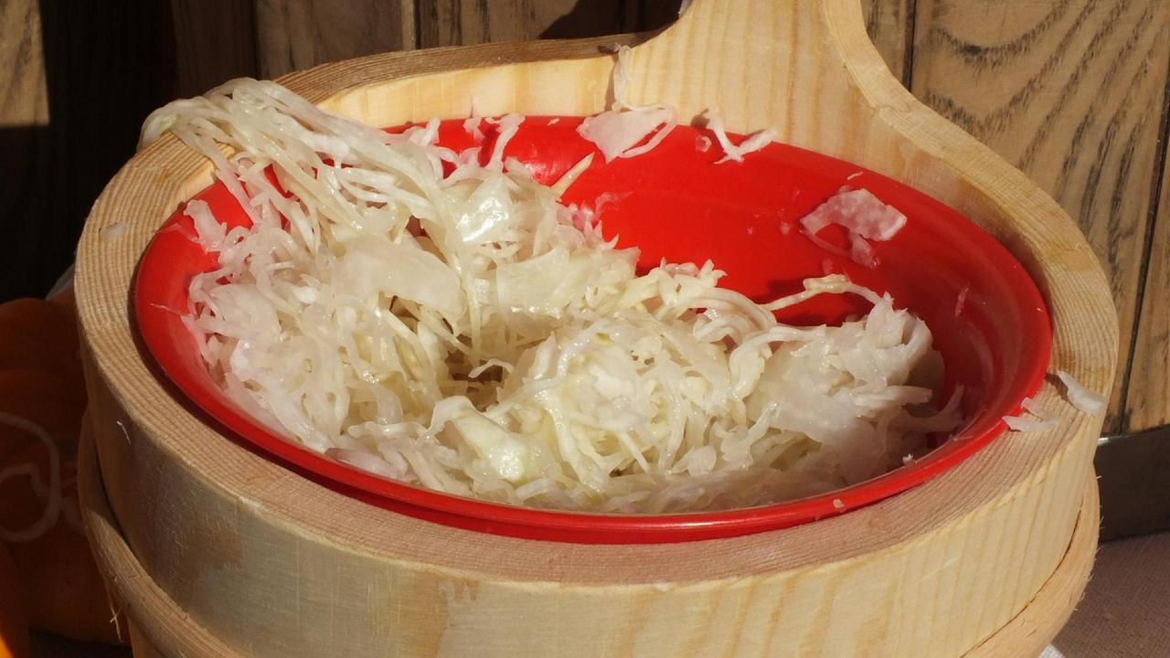 Ein Sauerkrauttopf aus Holz mit einem roten Sieb in dem frisches Sauerkraut liegt.