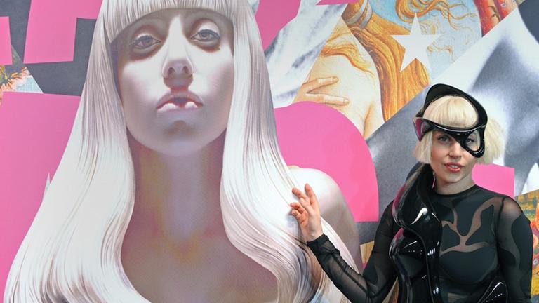 Die Musikerin Lady Gaga posiert in einem schwarzen Lederkostüm neben einem Bildnis von ihr, das der Künstler Jeff Koons angefertigt hat.
