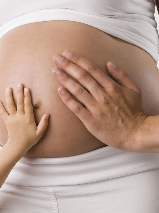 Zwei Hände berühren den Bauch einer Schwangeren.
