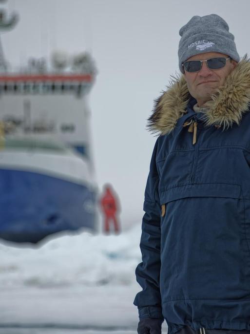 Markus Rex in Schutzkleidung mit der "Polarstern" im Hintergrund
