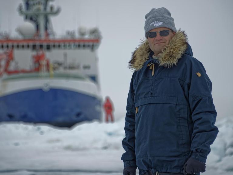 Markus Rex in Schutzkleidung mit der "Polarstern" im Hintergrund