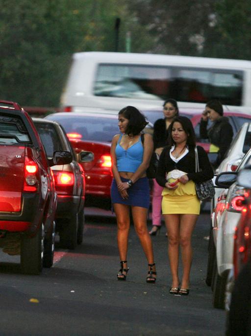 Prostituierte stehen auf einem Straßenstrich zwischen Autos.