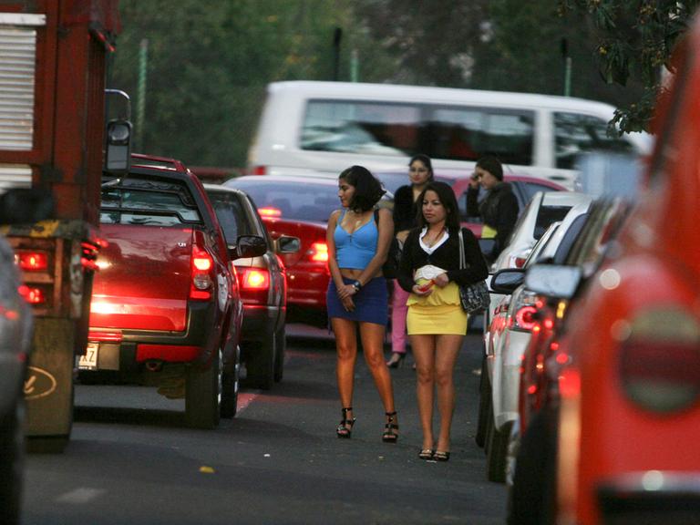 Prostituierte stehen auf einem Straßenstrich zwischen Autos.