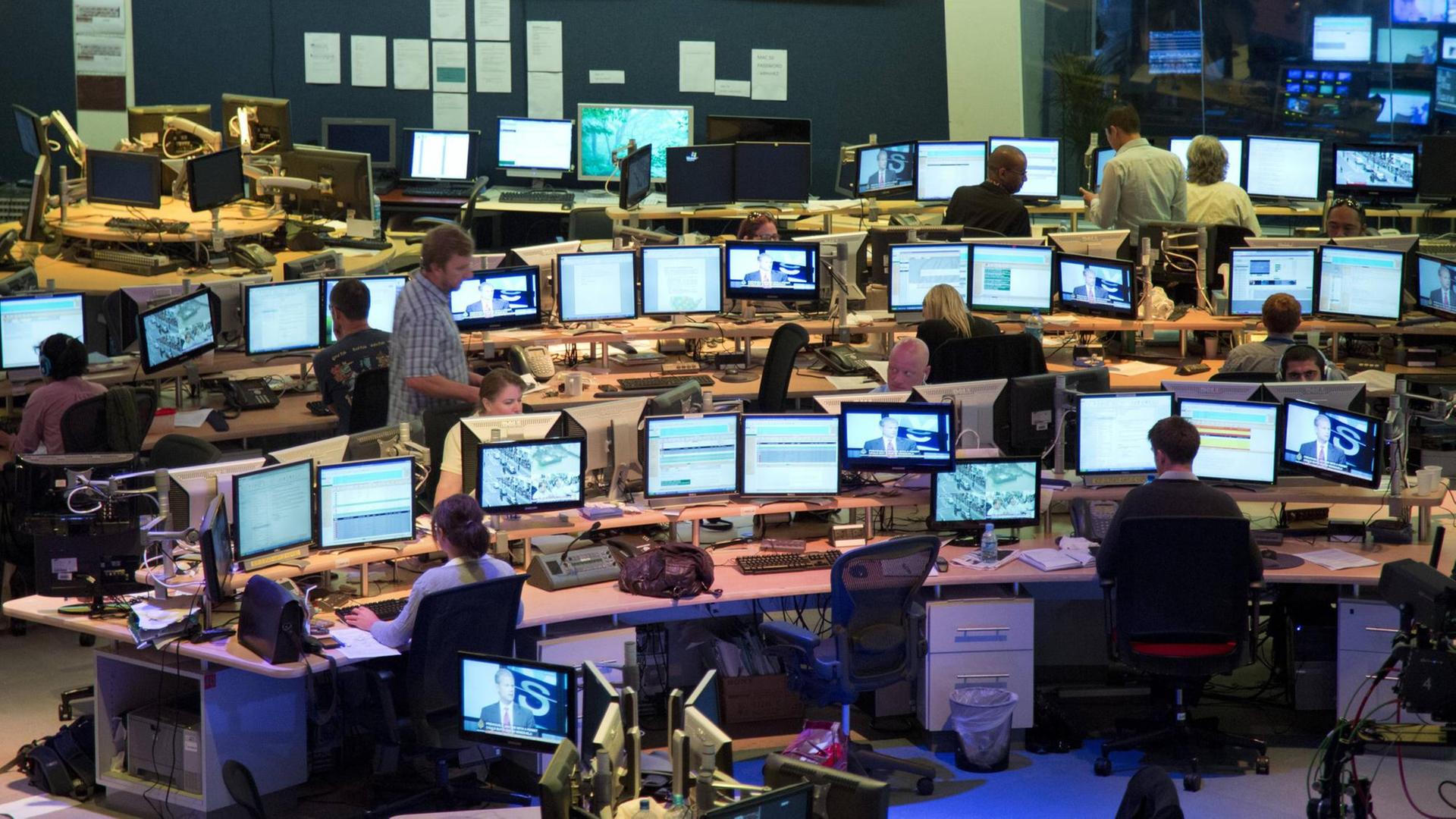 Symbolbild: Im Newsroom eines Fernsehsenders sitzen Journalisten hinter Bildschirmen und arbeiten.