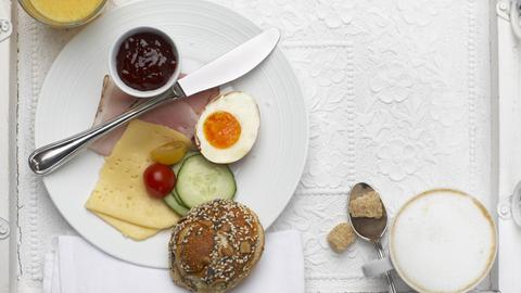 Frühstücksteller mit Brötchen, Ei, Marmelade, Käse, Schinken und Gurkenscheiben - mit Kaffee und Orangensaft