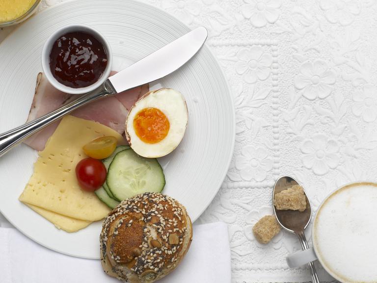 Frühstücksteller mit Brötchen, Ei, Marmelade, Käse, Schinken und Gurkenscheiben - mit Kaffee und Orangensaft