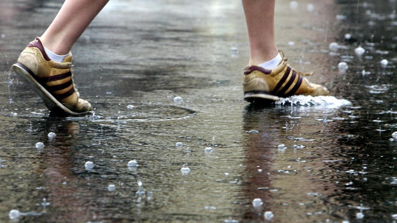 Die Schuhe einer Fußgängerin auf einer regennassen Straße in der Innenstadt von Frankfurt.