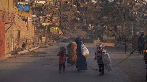 Eine Frau schleppt zusammen mit ihren Kindern Säcke über die Straße.