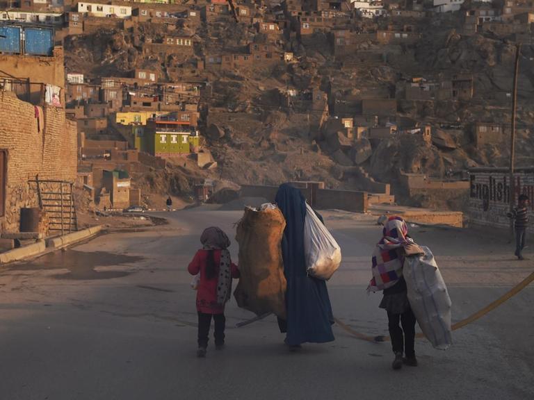 Eine Frau schleppt zusammen mit ihren Kindern Säcke über die Straße.
