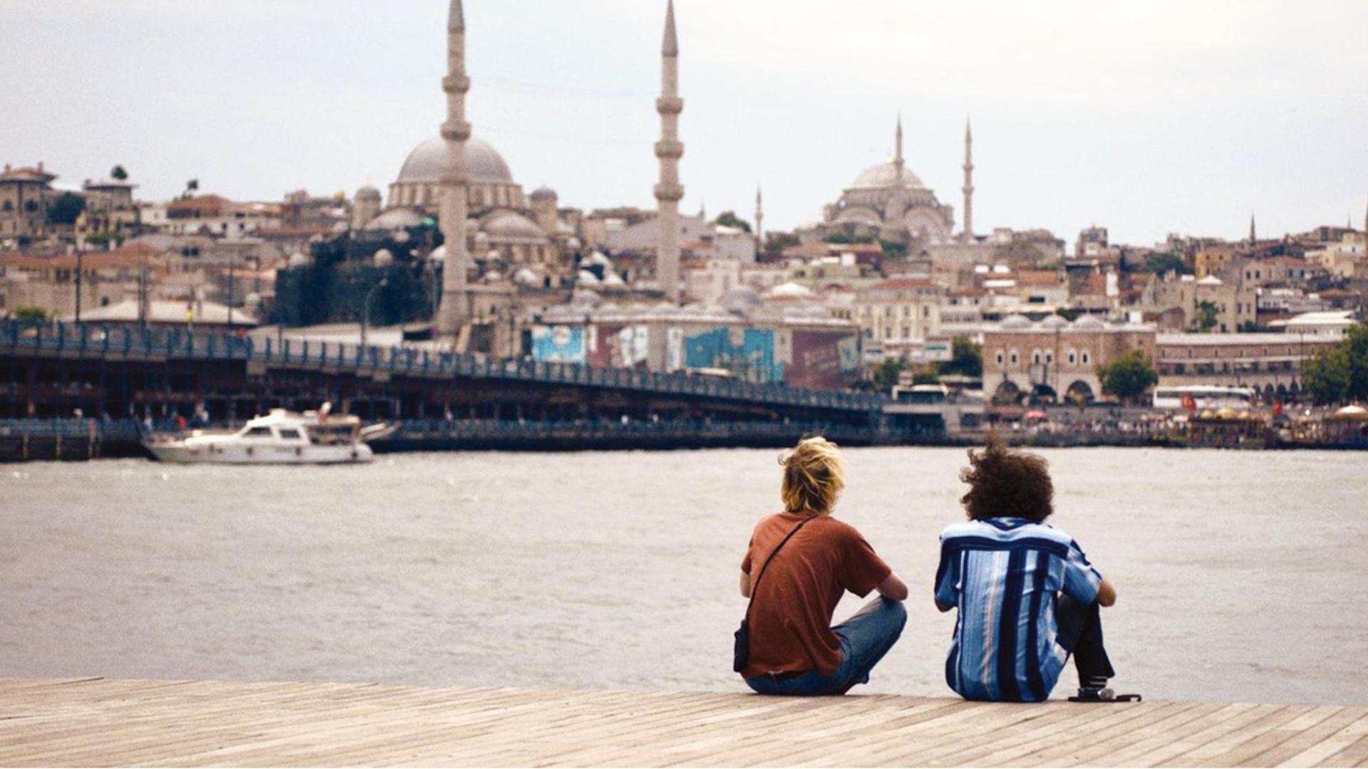 Zwei junge Männer sitzen vor der Skyline von Istanbul.