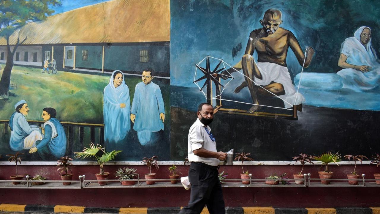 An einem Gebäude ist ein Bild von Gandhi gemalt, ein Mann geht daran vorbei.