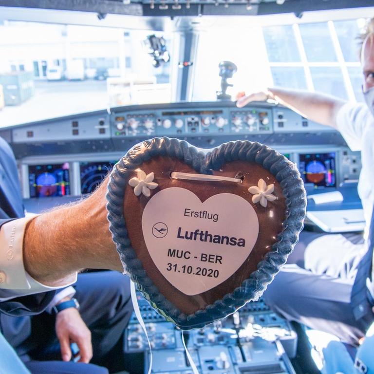 Eröffnung des BER-Airports: Lufthansa Pilot Peter Etzrot und sein Co-Pilot Kai Schleicher halten im Cockpit eines Airbus vom Typ A320neo ein Lebkuchenherz mit der Aufschrift "Erstflug Lufthansa MUC-BER 31.10.2020" in der Hand. 