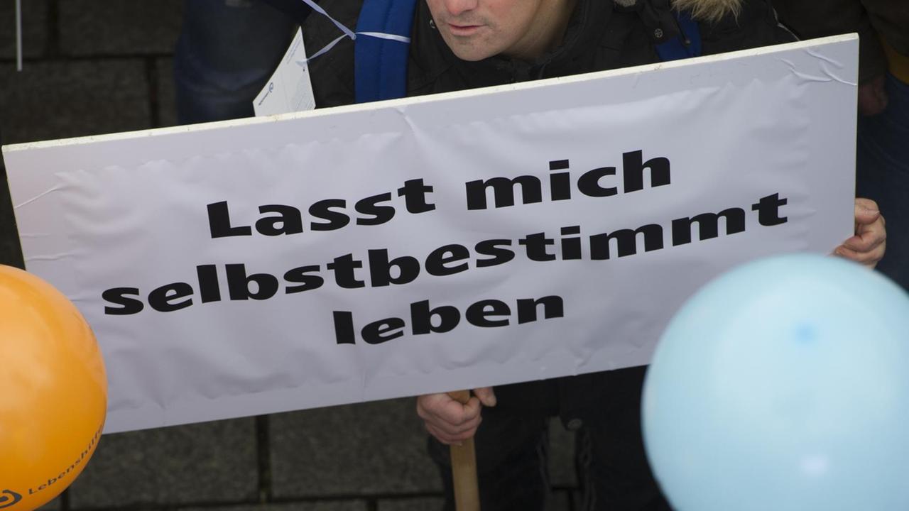 "Lasst mich selbstbestimmt leben" steht am 07.11.2016 in Berlin auf dem Plakat eines Demonstranten vor dem Brandenburger Tor. Die Bundesvereinigung "Lebenshilfe" hatte zu einer Demonstration aufgerufen, um ein besseres Bundesteilhabegesetz (BTHG) für Menschen mit Behinderung zu fordern. Derzeit befassen sich bundespolitische Gremien mit der künftigen Gestaltung des neuen BTHG. Foto: Paul Zinken/dpa ++