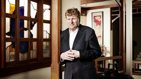 Ein Mann steht in einem Zimmer mit Holzbalken, er lehnt sich an eine Holzsäule