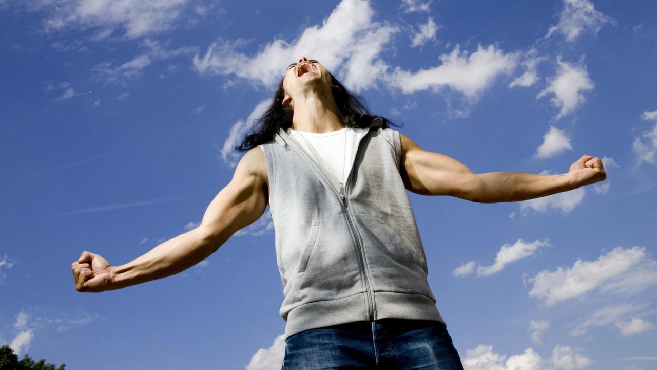 Ein Mann mit ausgebreiteten Armen und angespannten Muskeln schreit aus Leibeskräften gen Himmel.