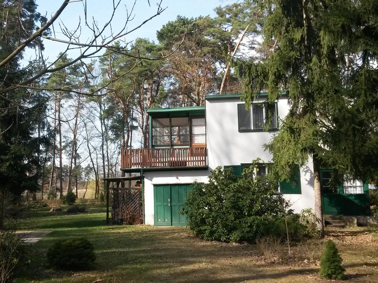 Weißes Haus mit grünen Türen und Holzbalkon in einem Garten