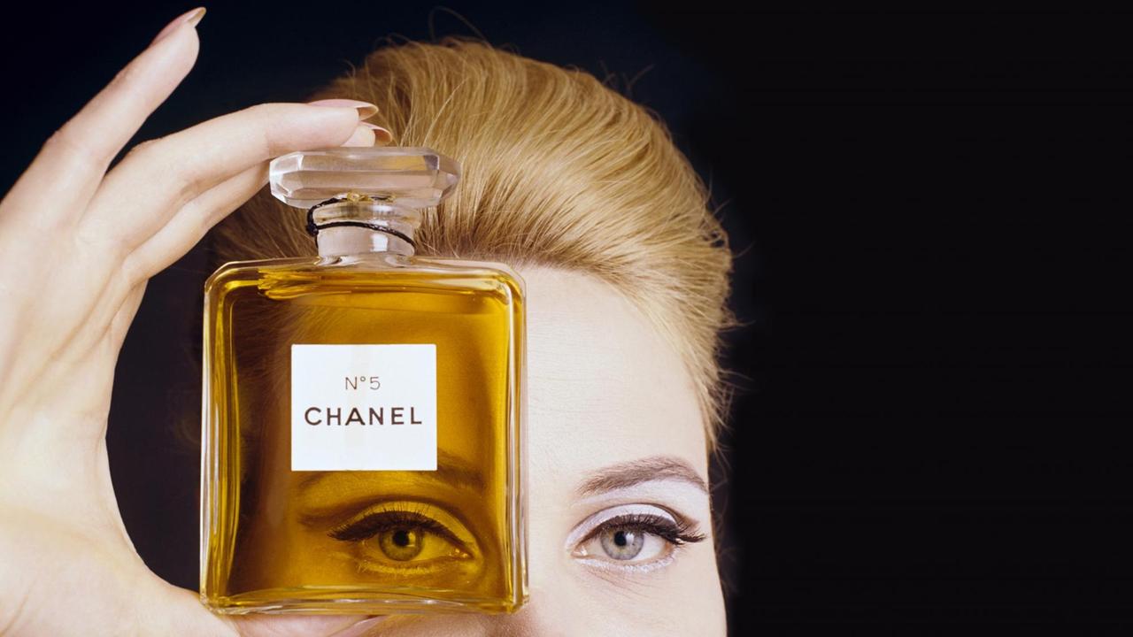 Nahaufnahme einer Frau, die eine Flasche des Chanel No.5 Parfüms vor ihrem Auge hält und durch sie durchschaut.