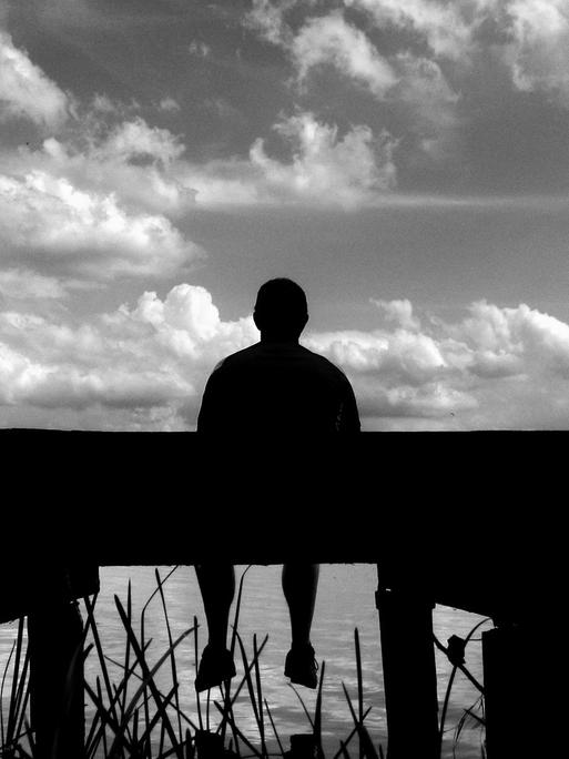 Ein Mann sitzt am 04.08.2013 auf einem Steg am Selenter See (Schleswig-Holstein).