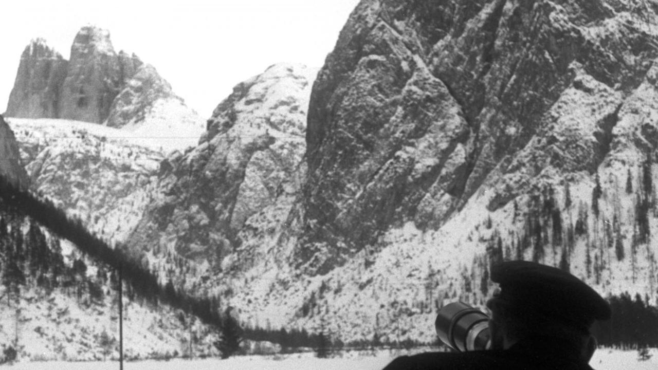 Beobachter stehen an der Straße zwischen Toblach und Cortina, die mit Fernrohren die drei Bergsteiger bei deren Aufstieg an der Nordwand der Großen Zinne verfolgen können. Im Hintergrund sieht man die aufragende Nordwand der Drei Zinnen (undatiertes Archivbild vom Januar 1963).