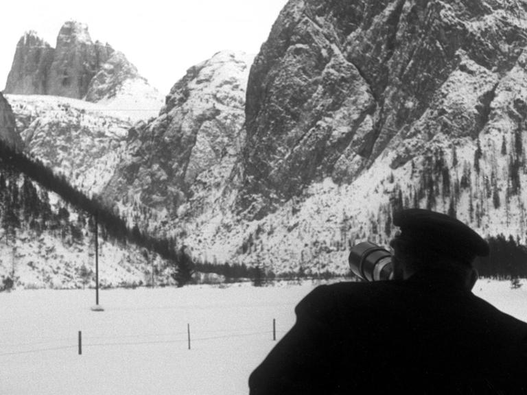 Beobachter stehen an der Straße zwischen Toblach und Cortina, die mit Fernrohren die drei Bergsteiger bei deren Aufstieg an der Nordwand der Großen Zinne verfolgen können. Im Hintergrund sieht man die aufragende Nordwand der Drei Zinnen (undatiertes Archivbild vom Januar 1963).