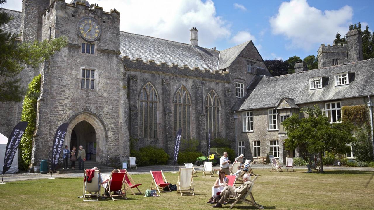 Menschen liegen in Liegestühlen vor dem gotischen Hauptgebäude von Dartington Hall.