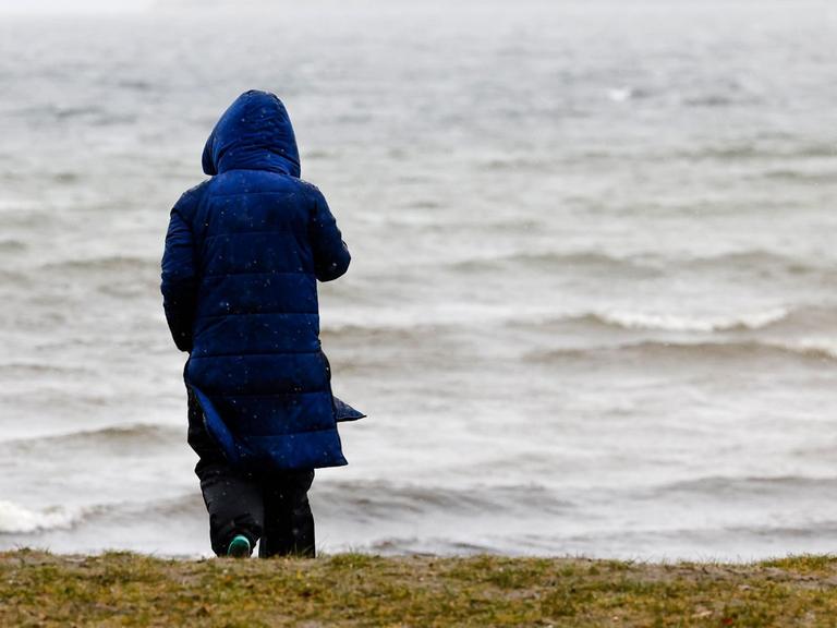 Eine Frau steht bei winterlichen Temperaturen und Regen an der Flensburger Förde.