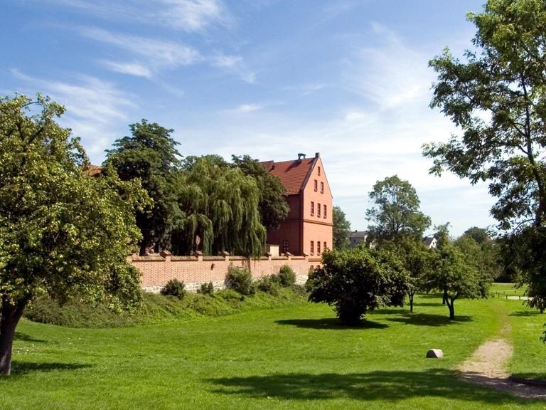 Ansicht der Alten Burg Penzlin und umliegender Wiesen an einem sonnigen Sommertag.