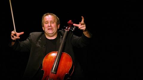 Der Kabarettist Matthias Deutschmann sitzt mit einem Cello auf der Bühne.