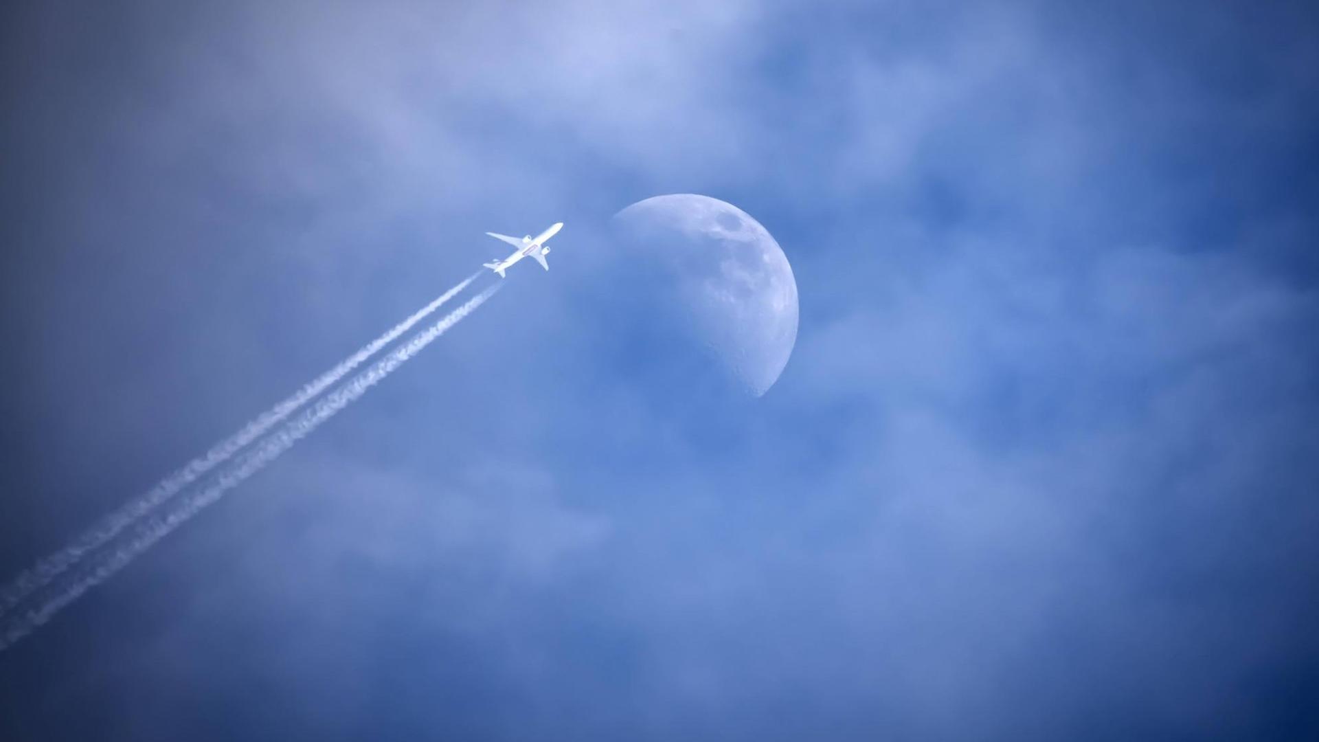 Flugzeug mit Kondensstreifen streift den Mond am Himmel.