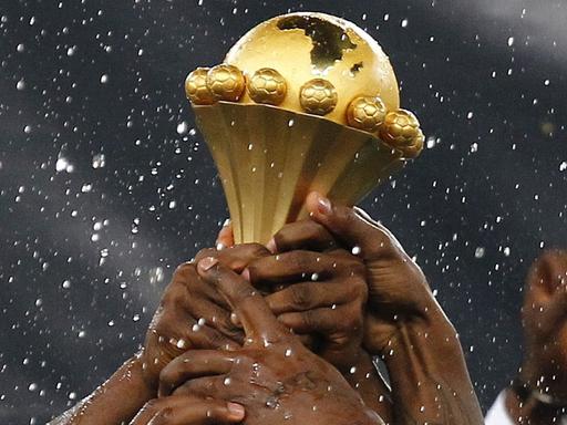 Mehrere Hände greifen nach der Trophäe des Afrika-Cups.