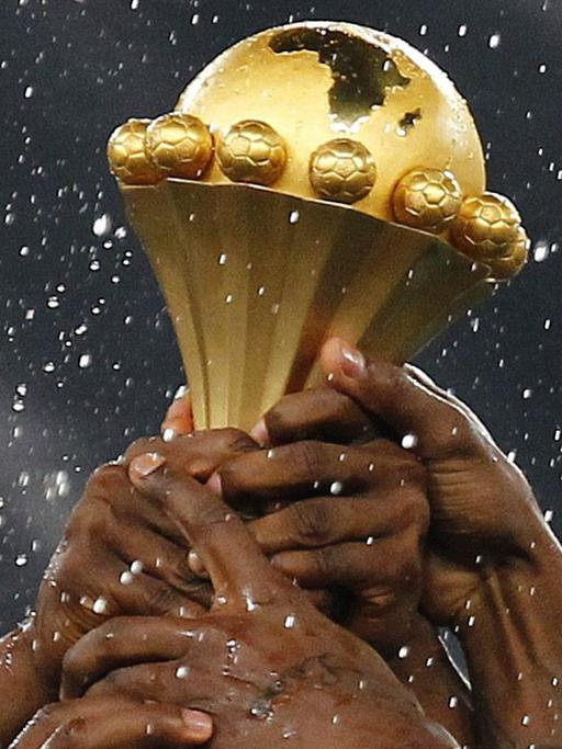 Mehrere Hände greifen nach der Trophäe des Afrika-Cups.