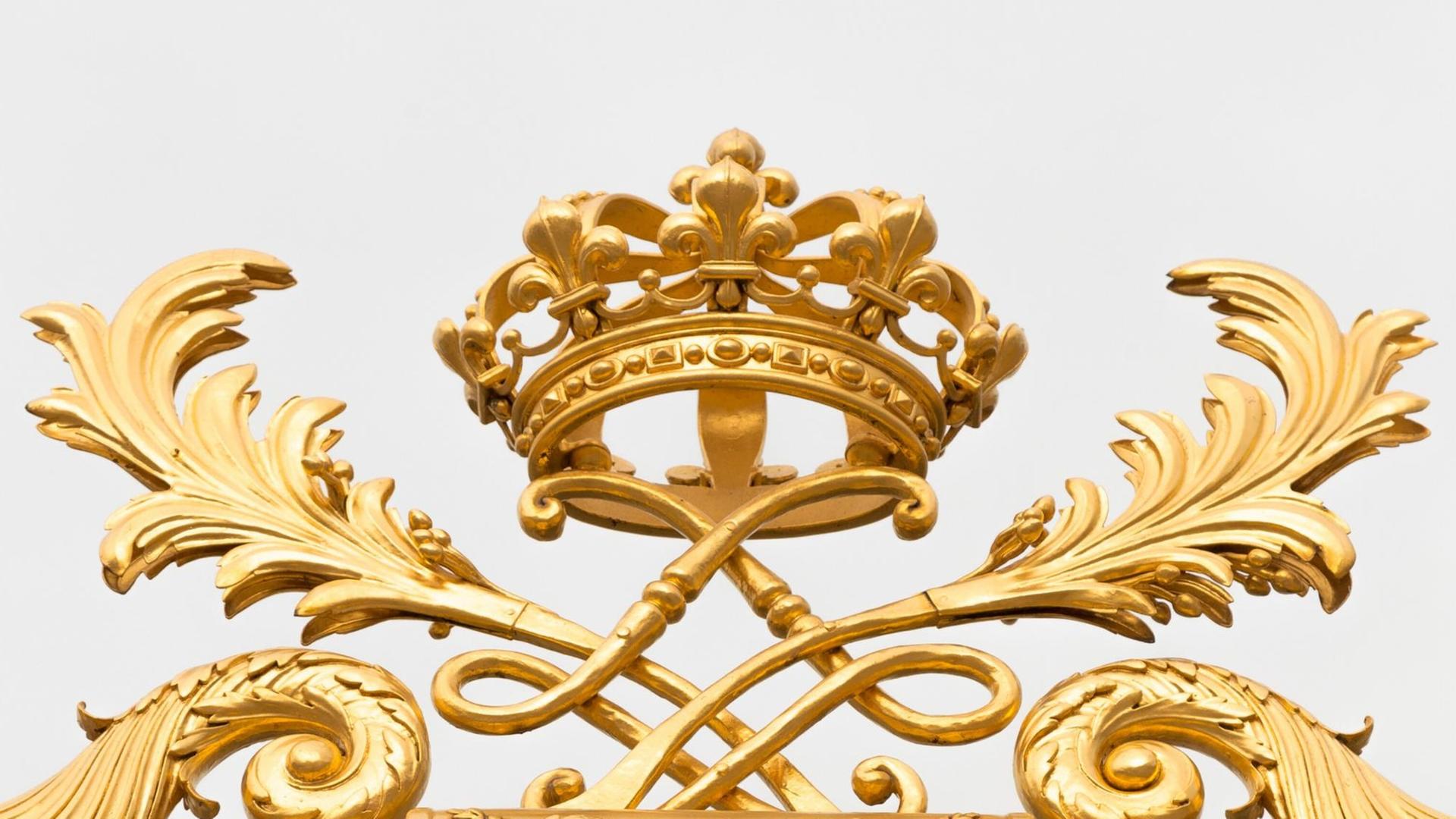 Eine goldene Kronen ist als Schmuck auf einem höfischen Palastzaun angebracht und vor blauem Himmel fotografiert.