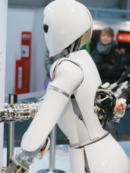 Ein Mitarbeiter des Robotic Innovation Centers steuert am 20.03.2017 bei der CeBIT Messe in Hannover (Niedersachsen) am Stand des deutschen Forschungszentrums für Künstliche Intelligenz (DFKI) mit Hilfe eines Exoskeletts den Roboter AILA.