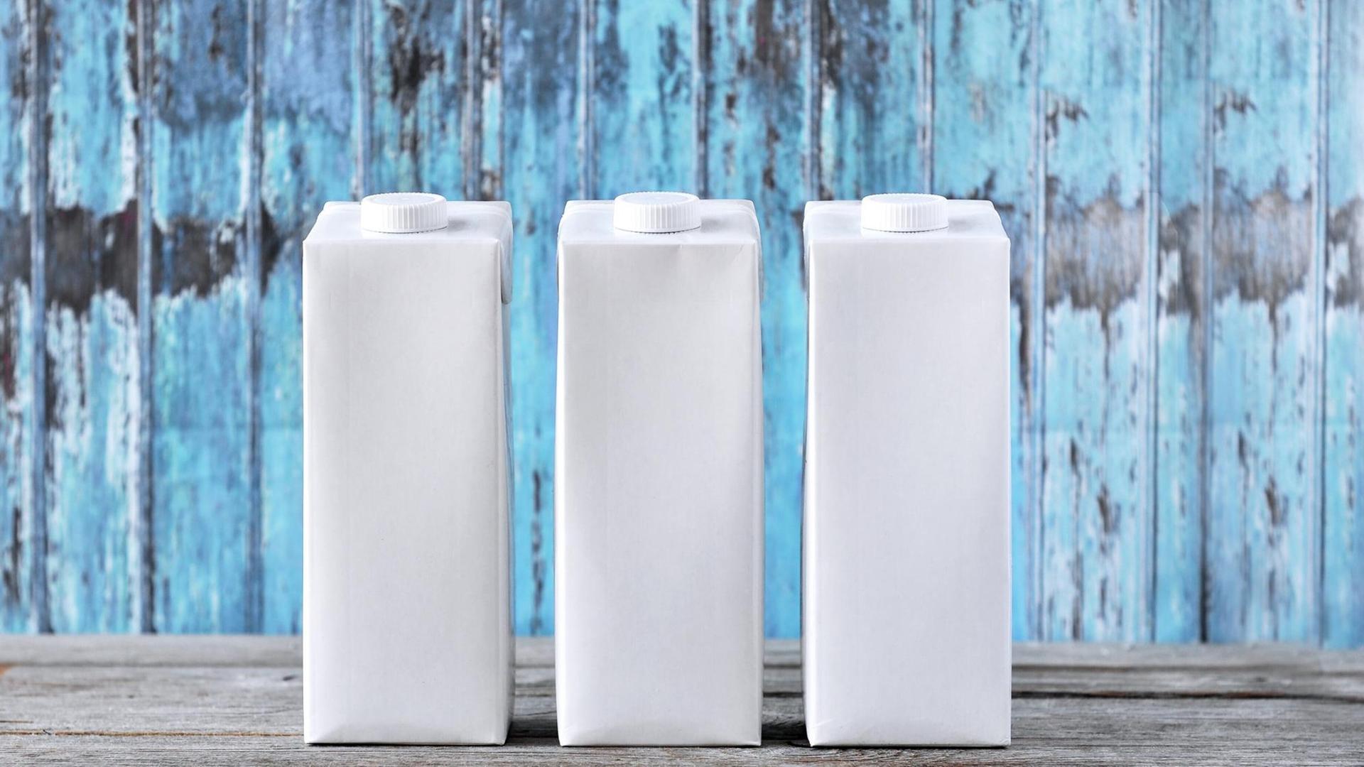 Drei weiße, unbedruckte Tetra Paks stehen auf einem Tisch vor blauem Hintergrund