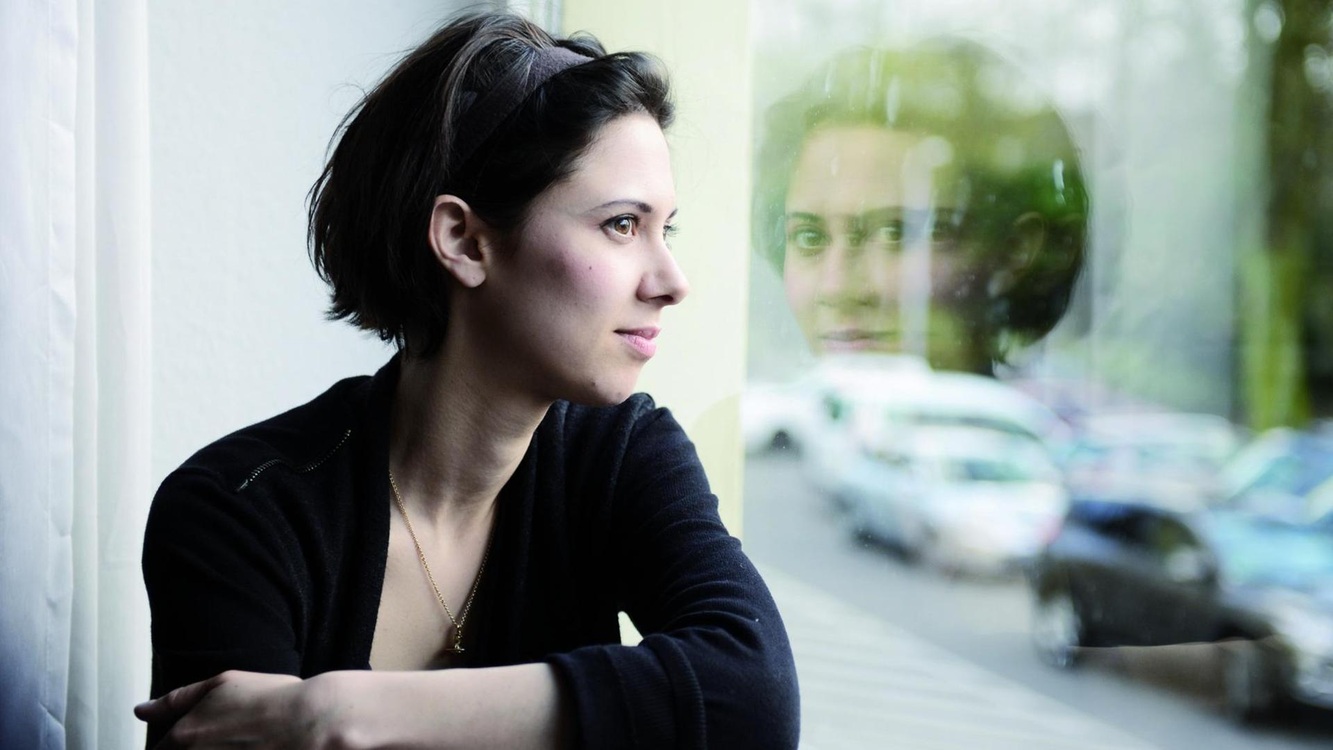 Die Pianistin Olivia Trummer schaut aus einem Fenster, in dem sich ihr Blick wiederspiegelt