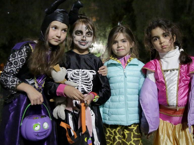 Kinder ziehen an Halloween abends im Dunkeln über die Straße, vier Kinder stehen nebeneinander verkleidet auf der Straße.