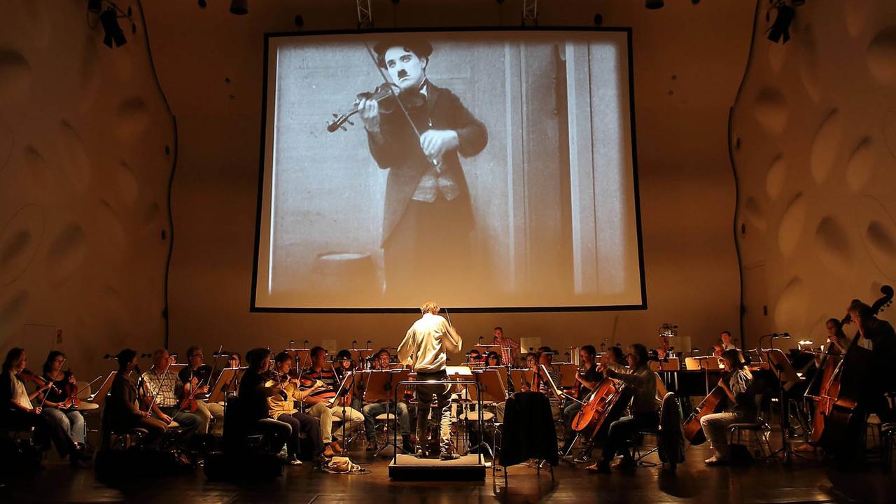 Das Filmorchester Babelsberg gibt ein Konzert in der Berliner Waldbühne. Im Hintergrund ist eine Szene aus einem "Harry Potter"-Film zu sehen, das Publikum verfolgt das Geschehen gebannt.