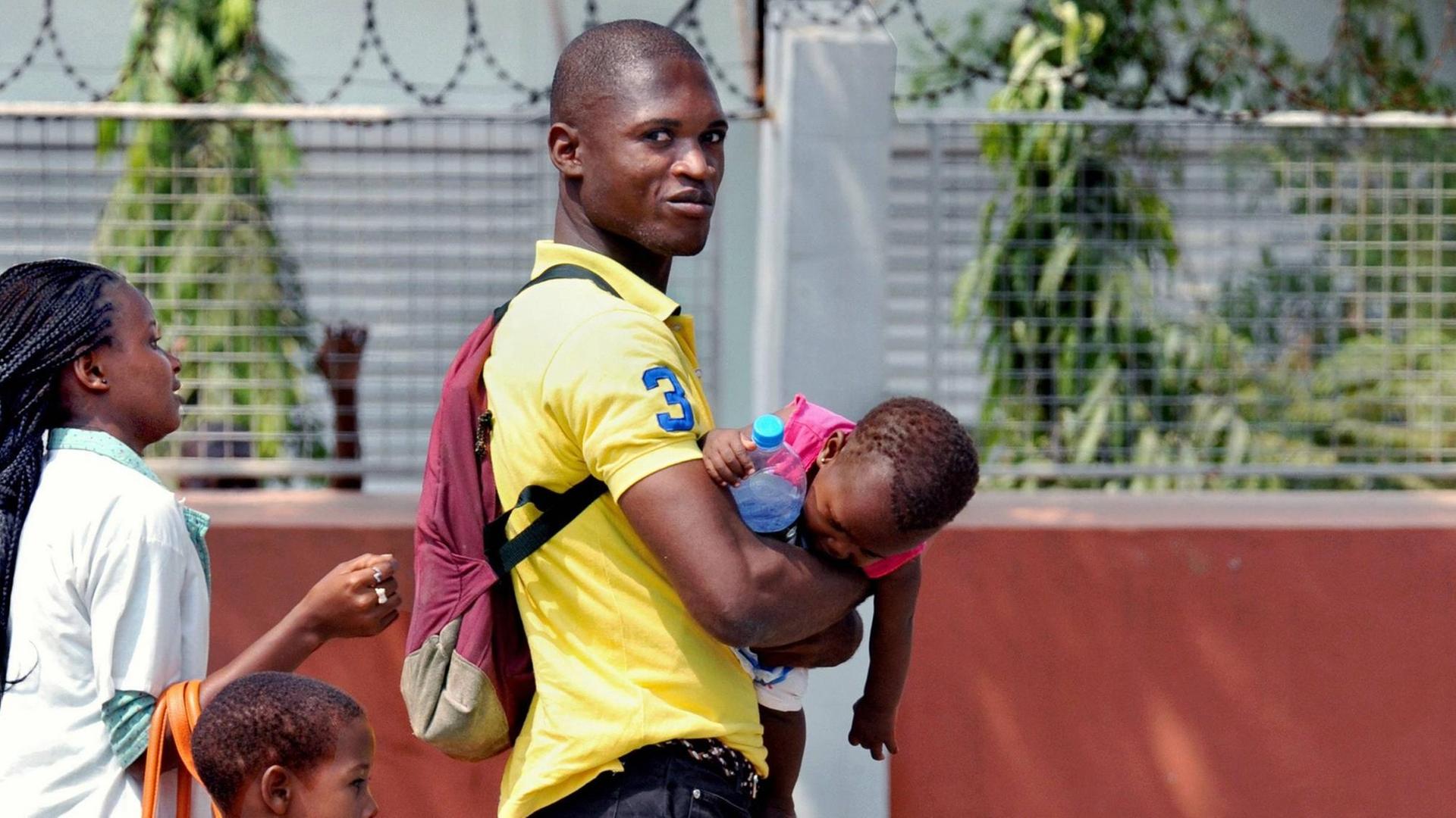 Ein Vater mit seinem Kind auf dem Arm, begleitet von seiner Frau und einem weiteren Kind auf der Straße in Luanda, Angola.
