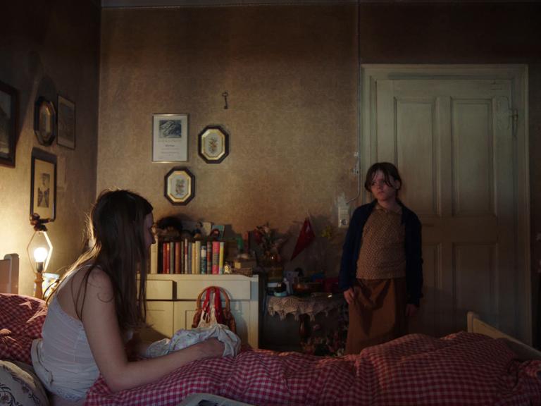 Szene aus dem Psychodrama "Fellwechselzeit" von Sabrina Mertens, das auf dem Festival Max-Ophüls-Preis Weltpremiere feierte. Eine Frau sitzt in einem Bett und ein Kind steht daneben.