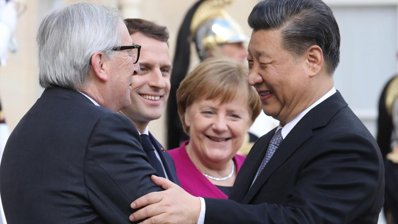 EU-Kommissionspräsident Jucker begrüßt den chinesischen Staatschef Xi. Im  Hintergrund sind Bundeskanzlerin Merkel und Frankreichs Präsident Macron zu sehen. 