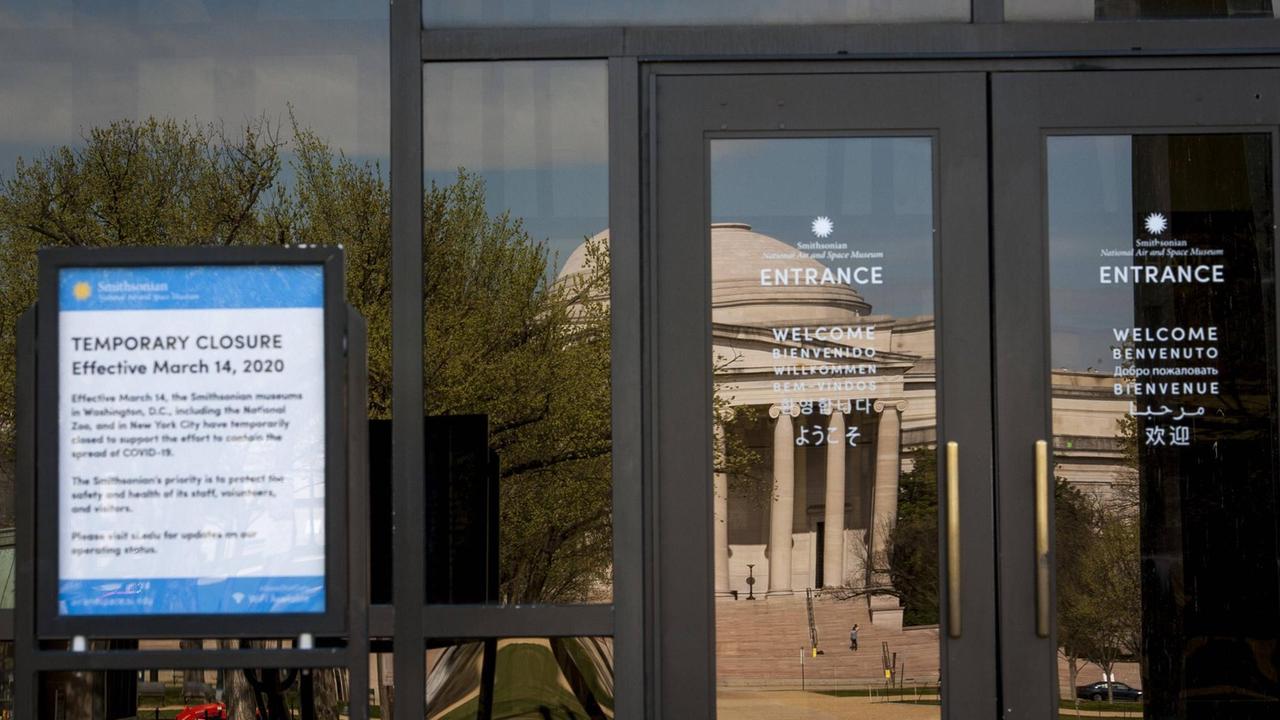Die Smithsonian National Gallery of Art spiegelt sich in der Glasfassade des  Smithsonian National Air and Space Museums. Beide sind wegen Corona geschlossen. Ein Hinweisschild erläutert Details.