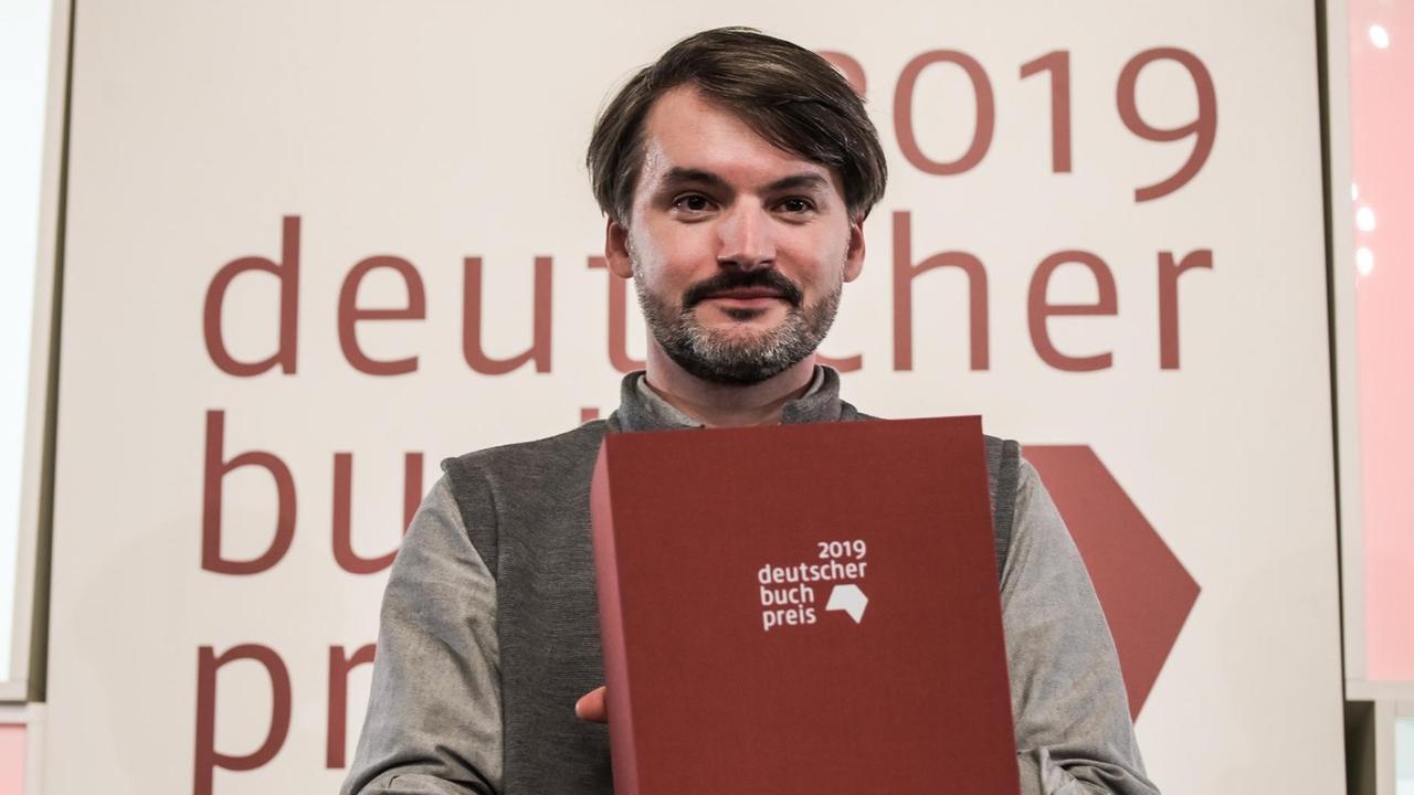 Saša Stanišić, aus Bosnien stammender Autor, erhält den Deutschen Buchpreis 2019 und steht am 14.10.2019 im Kaisersaal des Frankfurter Römers mit seiner Urkunde. Saša Stanišić, aus Bosnien stammender Autor, erhält den Deutschen Buchpreis 2019 und steht am 14.10.2019 im Kaisersaal des Frankfurter Römers mit seiner Urkunde.