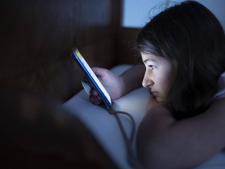 Ein Mädchen schaut im Bett auf sein Smartphone