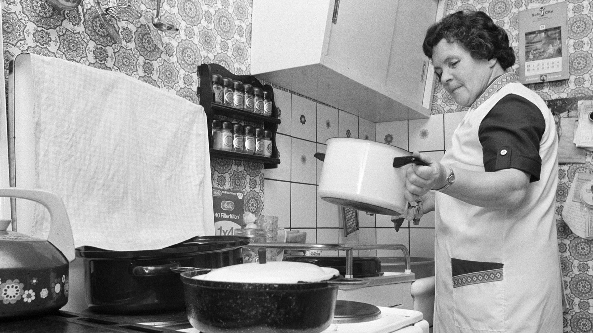 Eine ältere Frau bereitet an einem Herd das Essen zu - Deutschland in den 70ern.