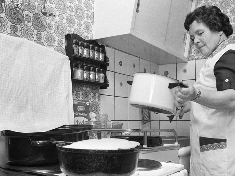 Eine ältere Frau bereitet an einem Herd das Essen zu - Deutschland in den 70ern.
