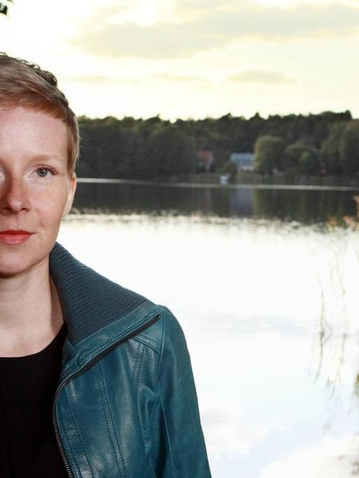 Die Autorin Judith Zander sitzt vor einem See und schaut in die Kamera.