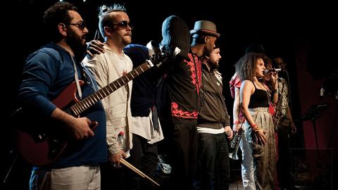 Acht Musiker der Hip Hop Band Nomadic Massive stehen auf einer Bühne und verabschieden sich beim Publikum