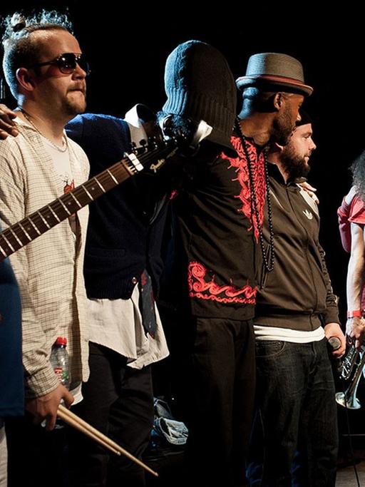 Acht Musiker der Hip Hop Band Nomadic Massive stehen auf einer Bühne und verabschieden sich beim Publikum