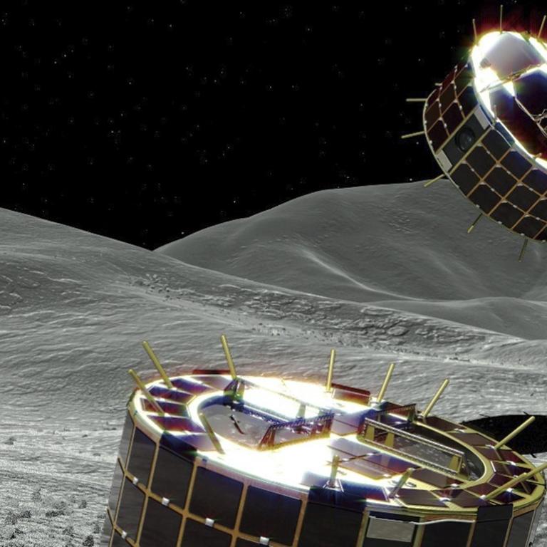 Die Computergrafik zeigt zwei zylinderförmigen und solarbetriebene Rover auf einem Asteroiden. 
